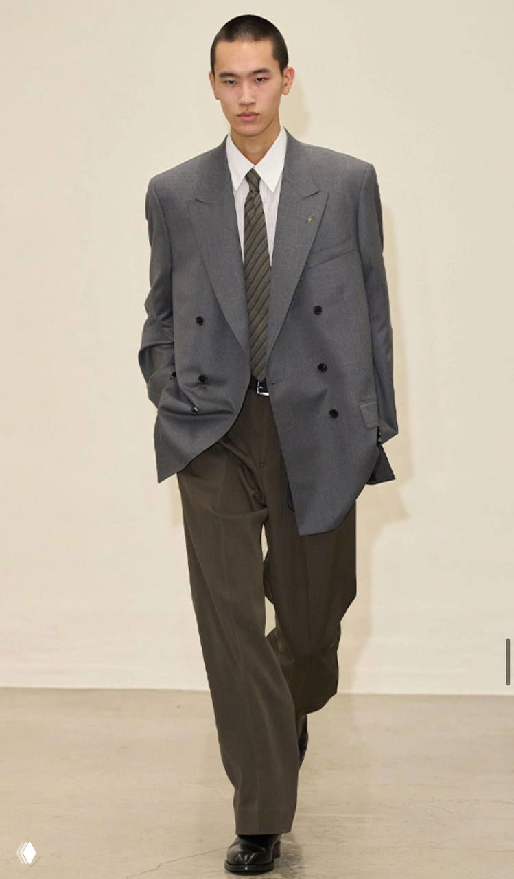 Модель в сером брючном костюме с двубортным пиджаком и свободными брюками: классический силуэт в актуальной серой гамме.