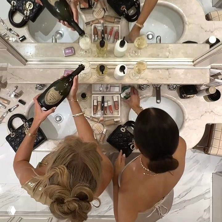 Вид сверху на туалетный столик с косметикой, зеркалом и аксессуарами; композиция в бежево-кремовых тонах, свечи и декоративные предметы.