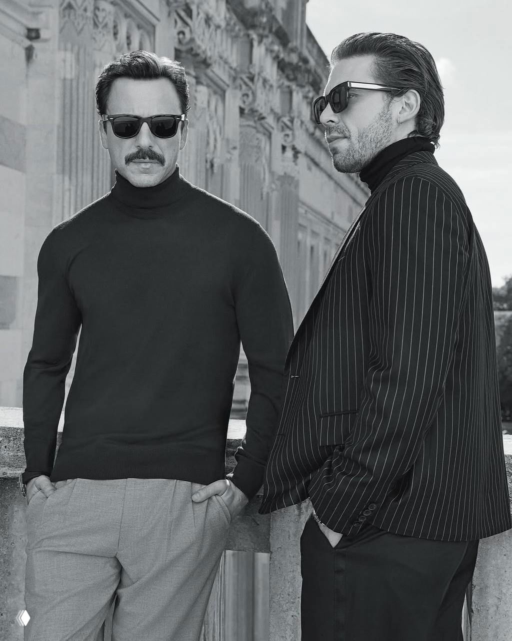 Чёрно‑белый портрет двух актёров в солнцезащитных очках и строгих образах на фоне архитектуры; кадр выдержан в ретро‑эстетике и минималистичной гамме.