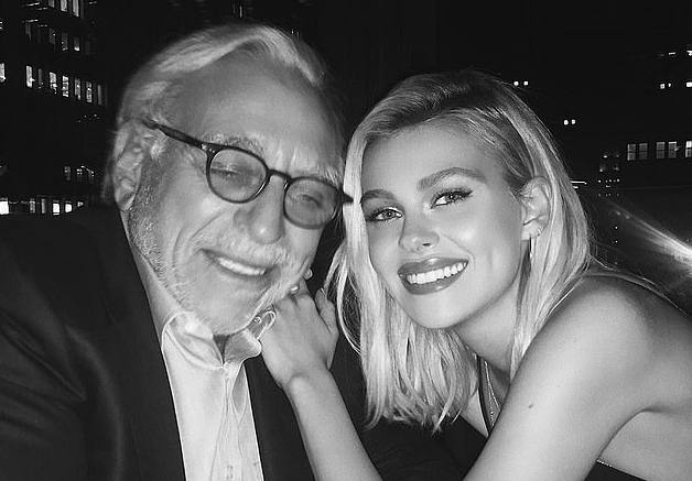 Чёрно‑белый портрет молодой женщины и пожилого мужчины в вечернем городском антураже; близкий кадр, улыбки и интимная дружеская поза.