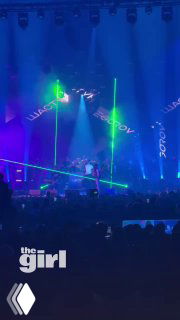 Сцена концерта VECHERINKA 2.0: артист на сцене, синие и зелёные лучи света, публика в зале; логотип канала «the girl» внизу.