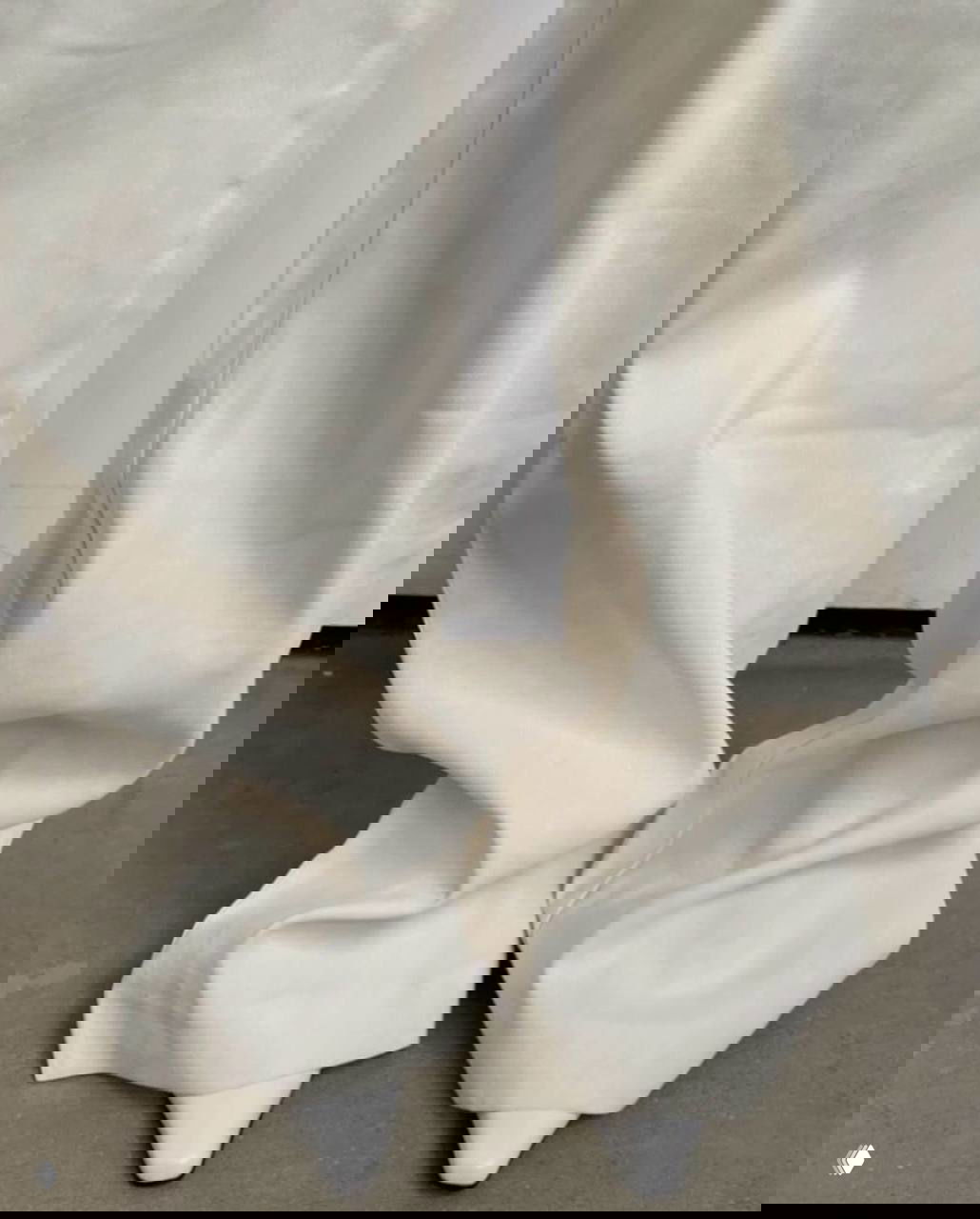 Нижняя часть образа: широкие светлые брюки и белые зауженные туфли на нейтральном фоне — пастельная фактура и складки ткани в оттенках белого.