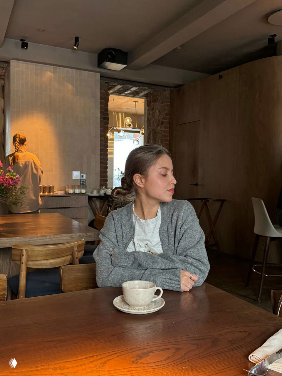 Девушка в уютном кафе в сером кардигане за чашкой кофе — кадр подсказывает идеи для спокойного образа и ухода за тканями перед зимой.