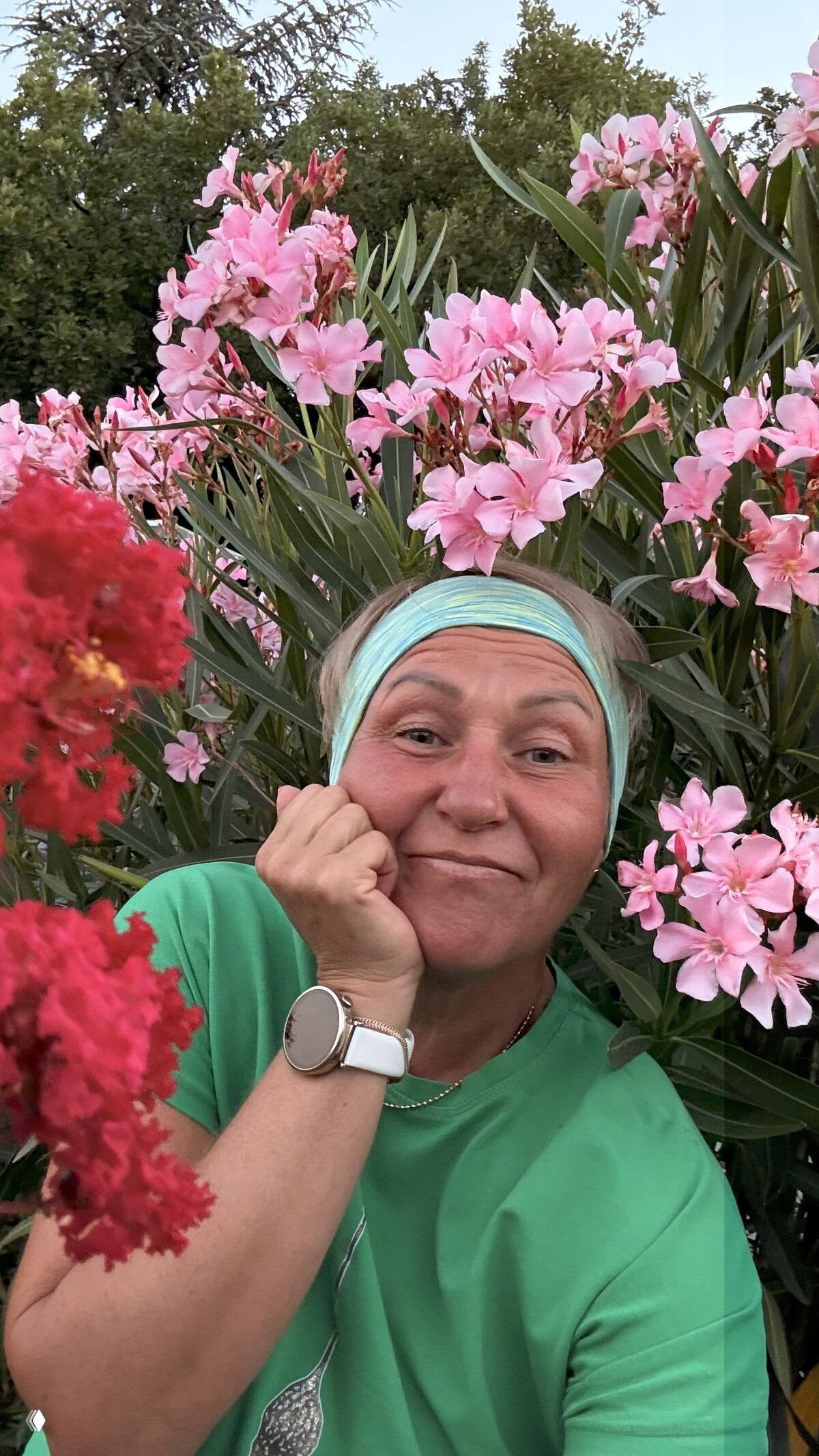 Портрет возле цветущих розовых олеандров: женщина позирует в окружении густых кистей цветов, летняя садовая сцена.