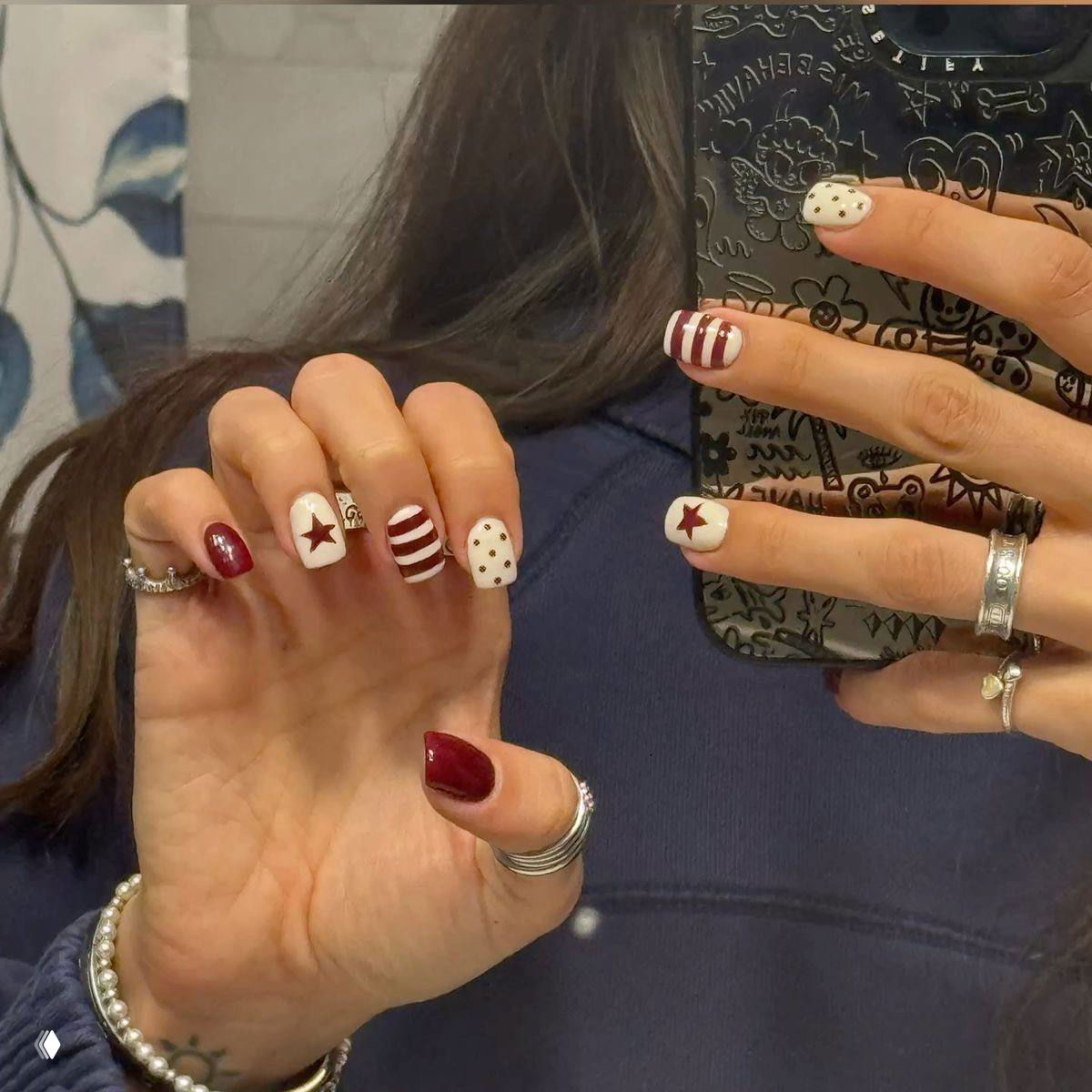 Зеркальное селфи рук с разным дизайном: белый с бордовыми полосами, звёздочки и горошек, на фоне тёмной одежды и телефона с рисунком.