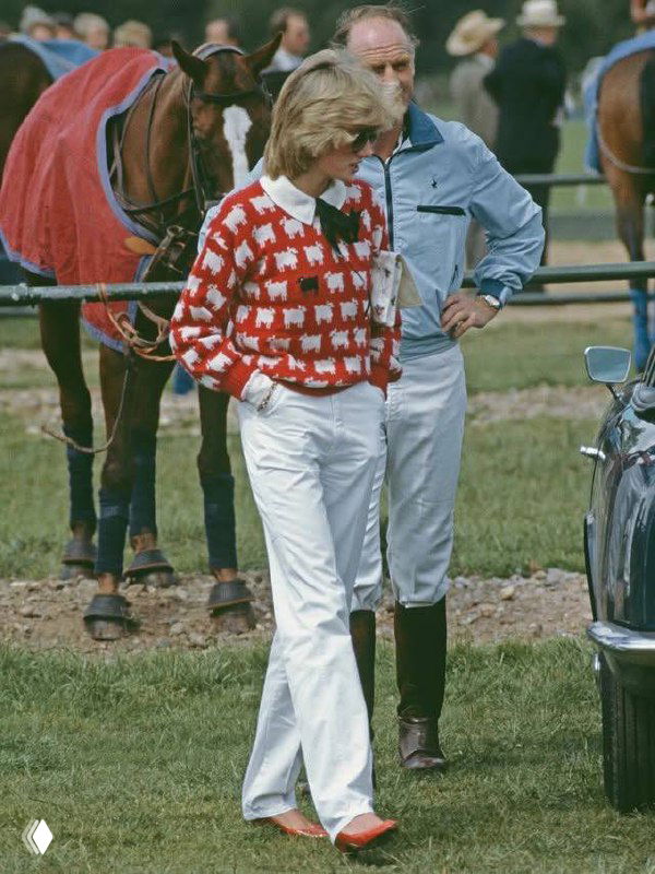 Архивное фото: женщина в красном свитере с белым узором овечек и белыми брюками на фоне поля и лошадей — ретро-образ для вдохновения.