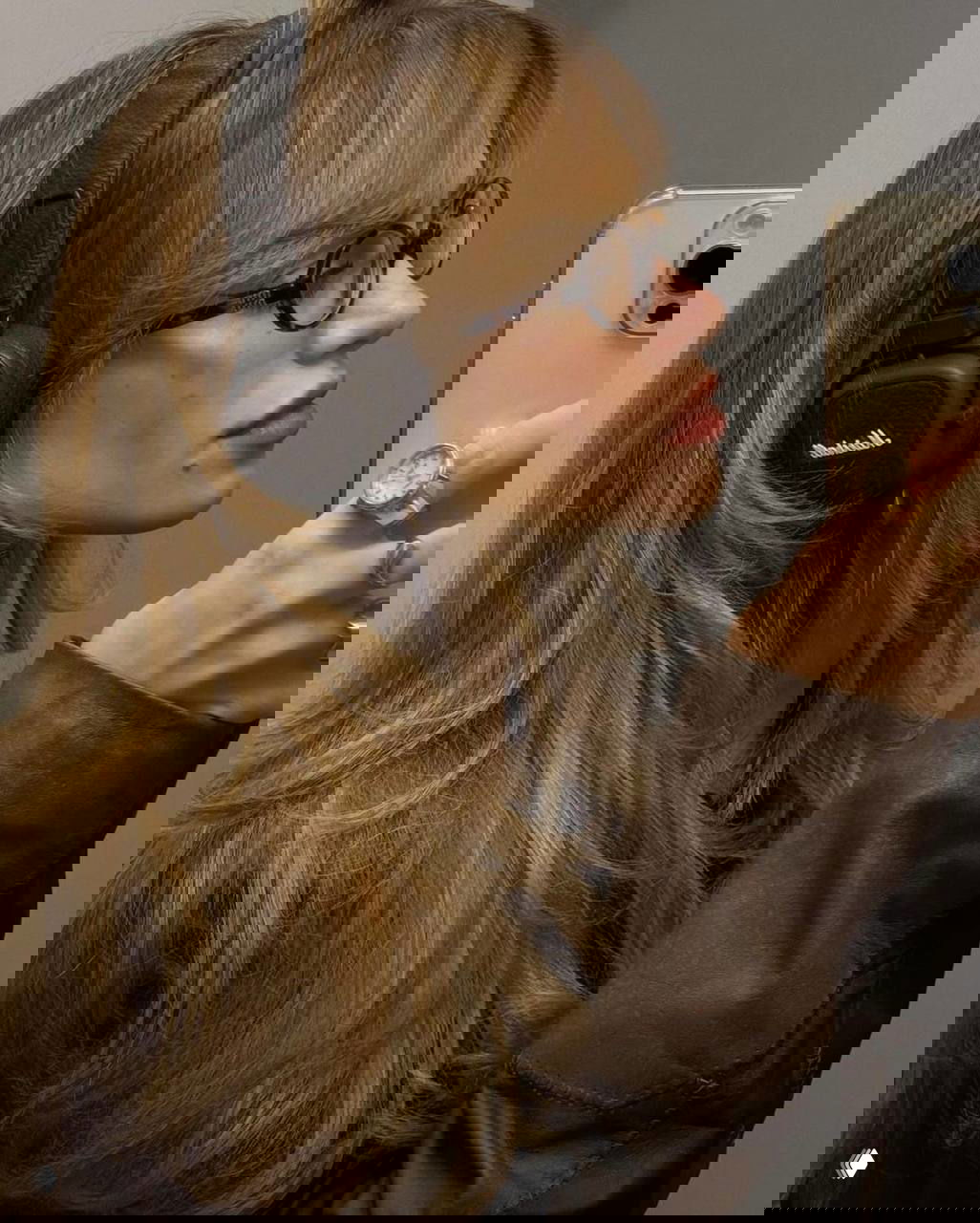 Профиль девушки в очках, делающей селфи в больших наушниках Marshall — пример стильного и мощного звука в подарке