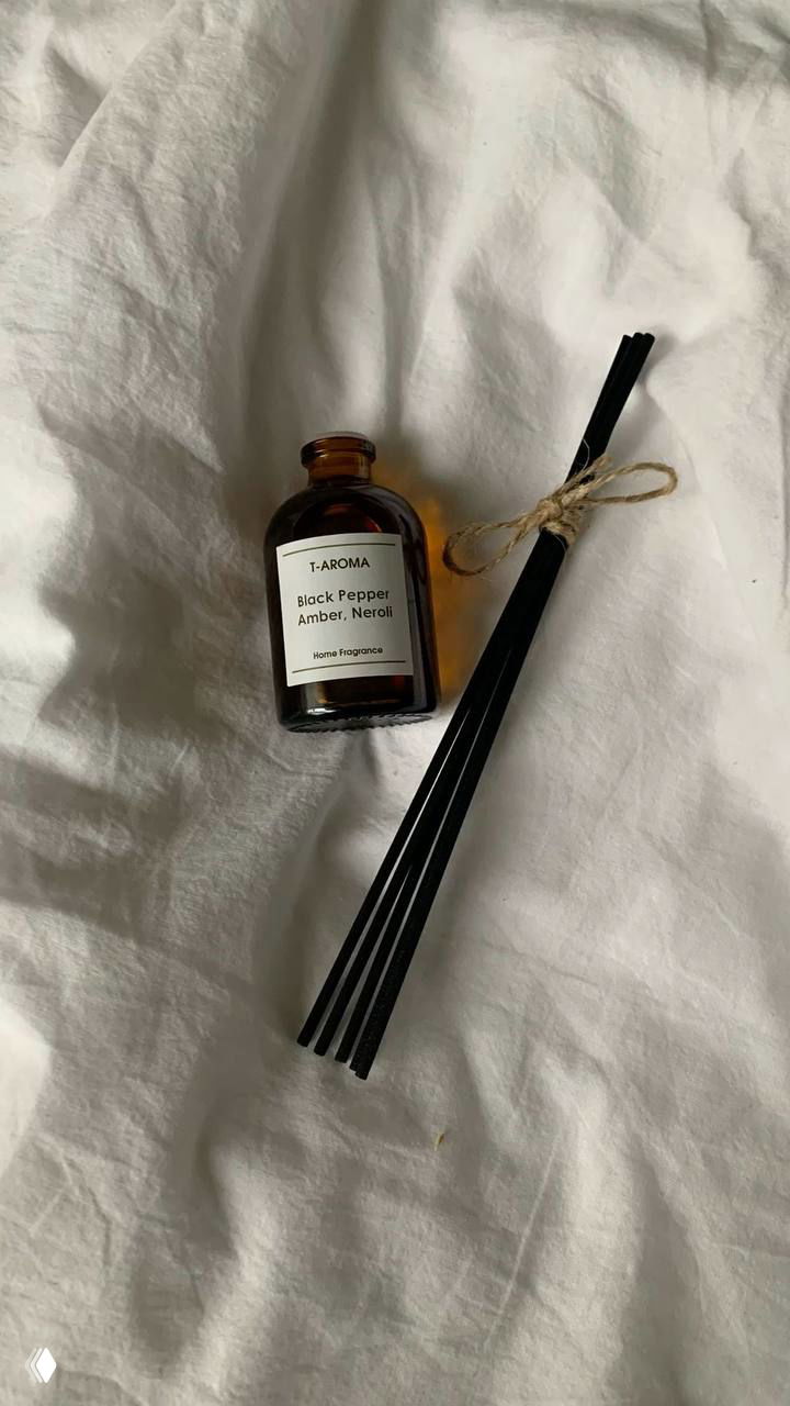 Минималистичный фото: флакон ароматического диффузора и черные палочки на белом постельном фоне — идея для уюта дома