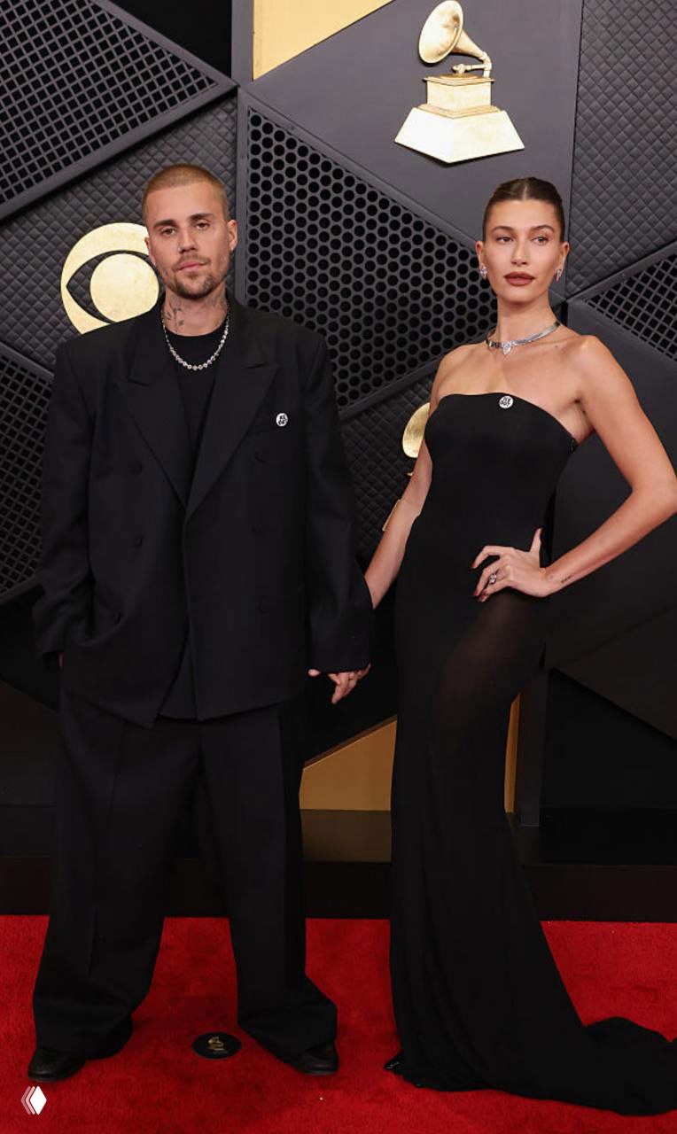 Дуэт: мужчина в свободном чёрном костюме и женщина в облегающем чёрном платье на красной дорожке «Грэмми», позируют вместе, видна изящная бижутерия.