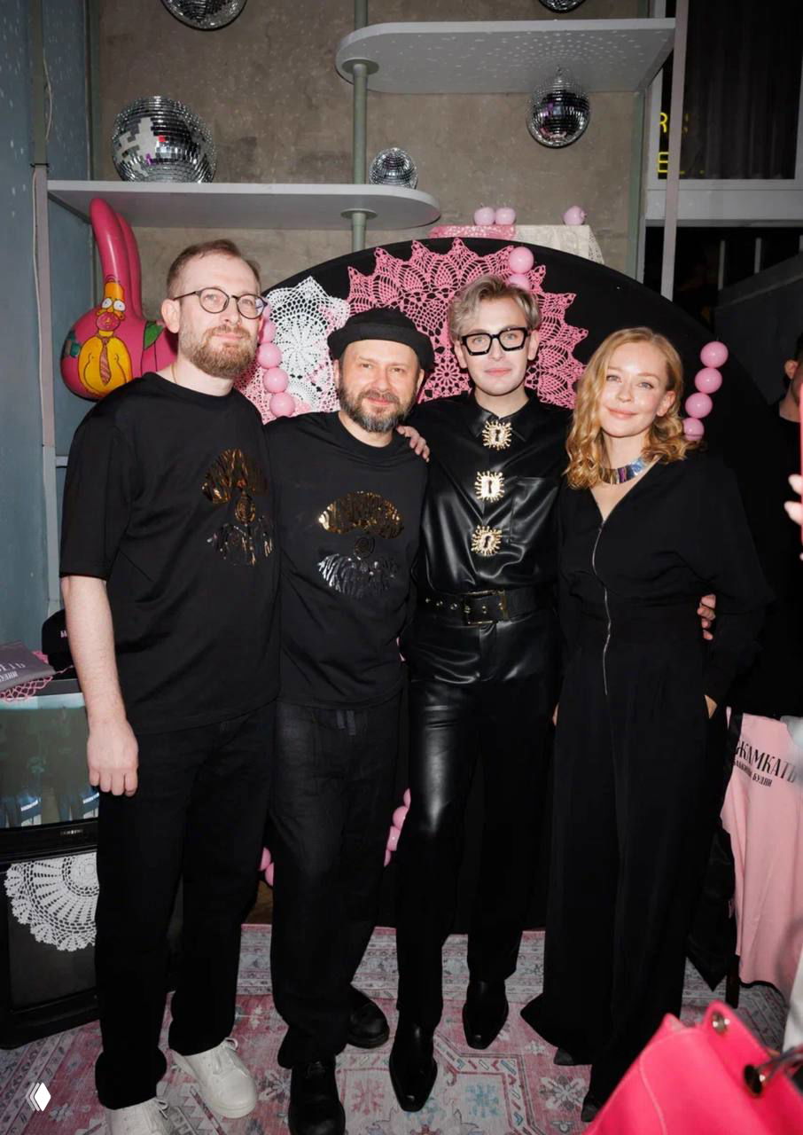 Групповое фото четырёх гостей у декоративной инсталляции: вечерняя атмосфера, разноцветная подсветка и непринуждённые позы на фоне розовых декоров.