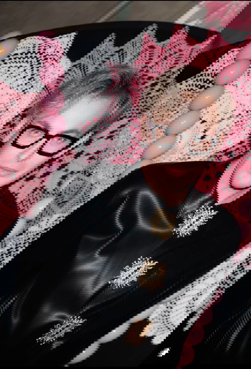 Портрет мужчины в кожаном наряде и больших тёмных очках, снятый на фоне розовой вязной декорации, бумажных шаров и интерьерной инсталляции в баре.