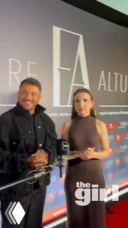 Фото с пресс‑вола: двое людей позируют перед баннером с именем Emre Altug, внизу виден логотип theGirl на мероприятии.