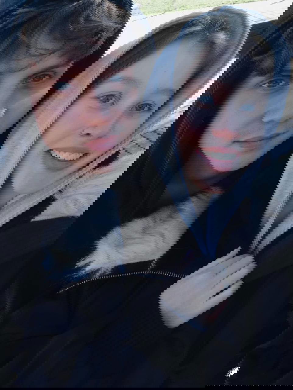 Уличное селфи пары в тёплой одежде: близкий план их лиц в капюшонах, дневное освещение, пара улыбается на свежем воздухе в прохладную погоду.