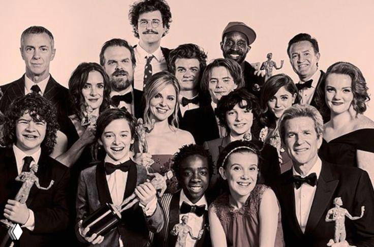 Чёрно‑белое групповое фото большой компании на красной дорожке/премьере: множество людей, праздничная атмосфера и позы для снимка.