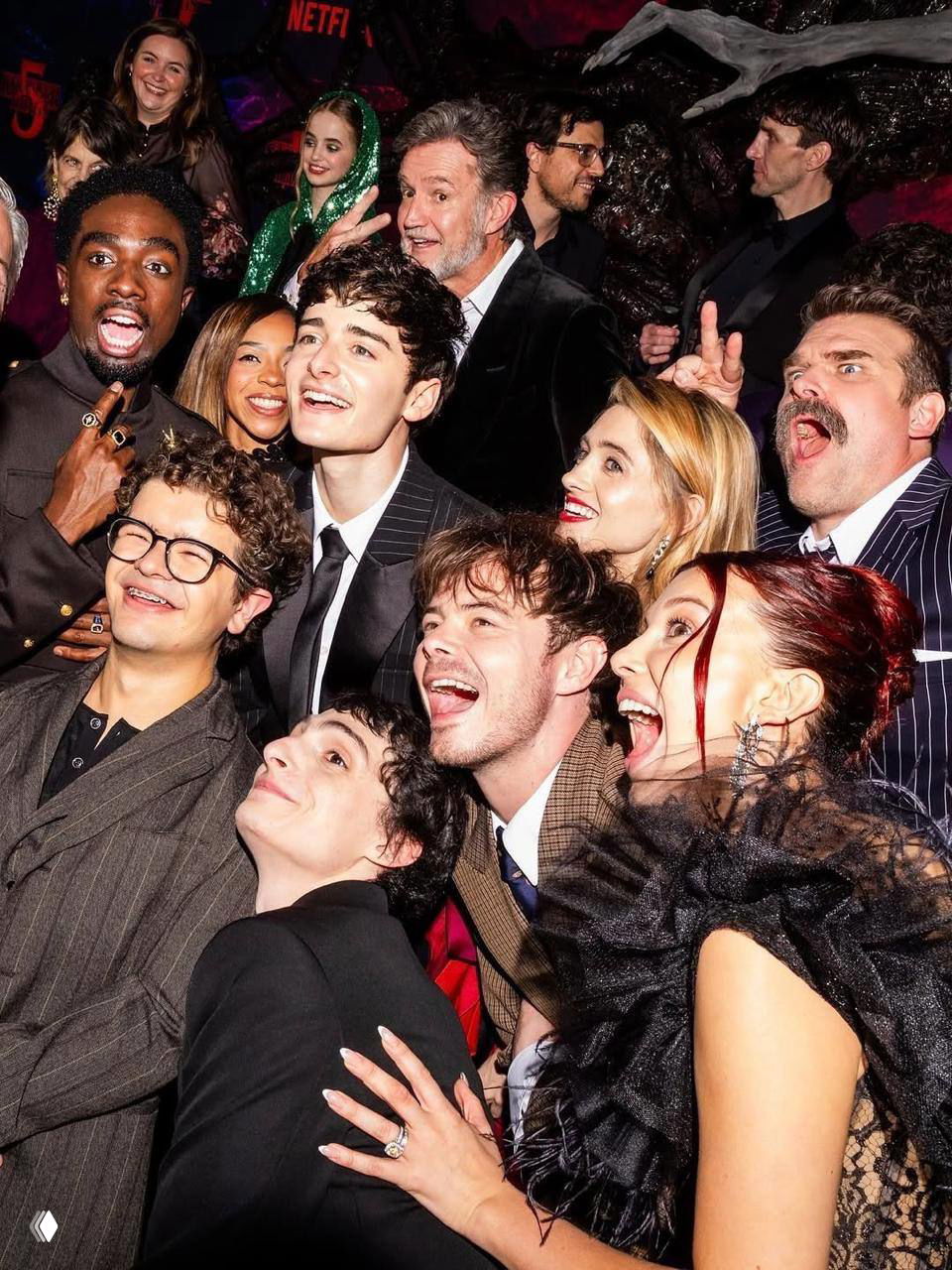 Яркое групповое фото со съёмочного или вечернего мероприятия: люди в вечерних нарядах, смех и тесные позы в кадре.