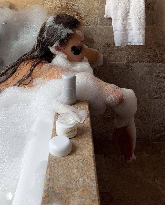 Интерьерный кадр ванны с пеной и баночками уходовой косметики на краю — вид на расслабляющий ритуал ухода и уютную атмосферу ванной комнаты.