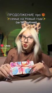 Кадр из видео: девушка сидит за столом и держит красиво упакованный подарок, в ролике показывает коробку и говорит о сумме для семьи.