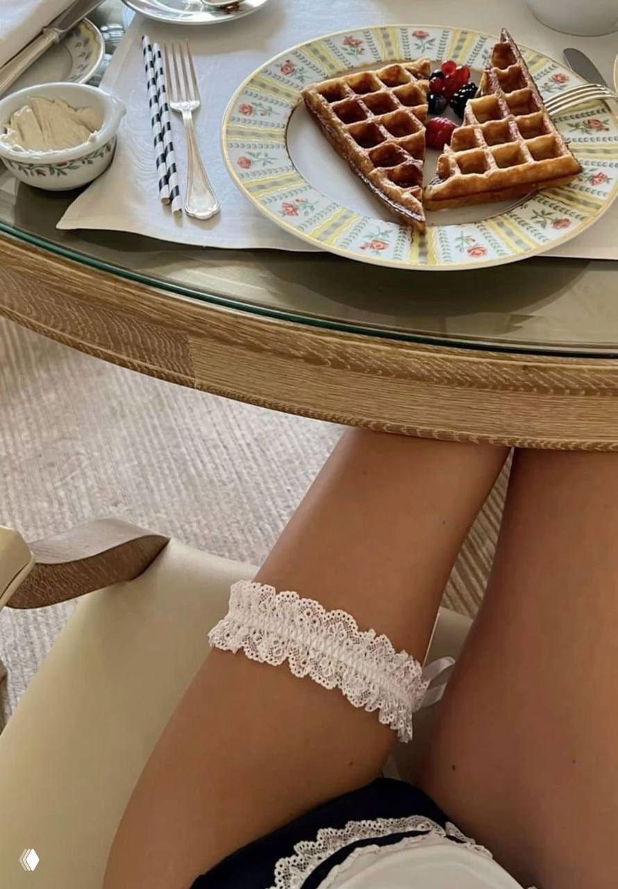Завтрак с вафлями на столе и ноги с кружевным аксессуаром под столом — эстетический кадр с романтическими деталями и утренней атмосферой.