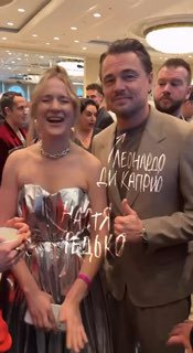 Кадр с гостями мероприятия: мужчина в тёмном костюме и женщина в нарядном платье позируют вместе в коридоре фуршета, окружённые другими посетителями.