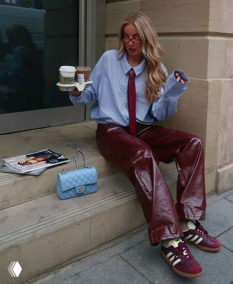 Девушка с кофейными стаканами в руках в небесно-голубой рубашке и бордовыми кожаными брюками, уличная сцена рядом с кафе.