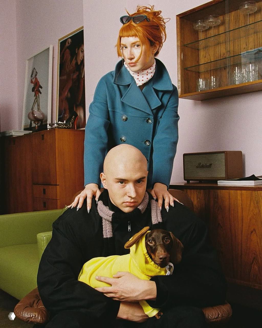 Кадр в студии: Лиза стоит над Сашей, он держит таксу в желтой одежде; ретро-мебель и стилизованная эстетика подчёркивают образ пары.