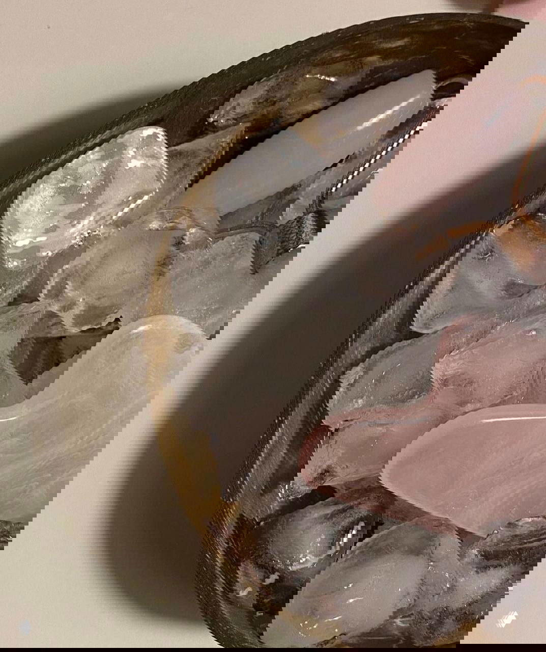 Розовый каменный гуаша и роллер в металлической миске со льдом на столе; крупный план инструментов для ухода за кожей и текстуры льда.