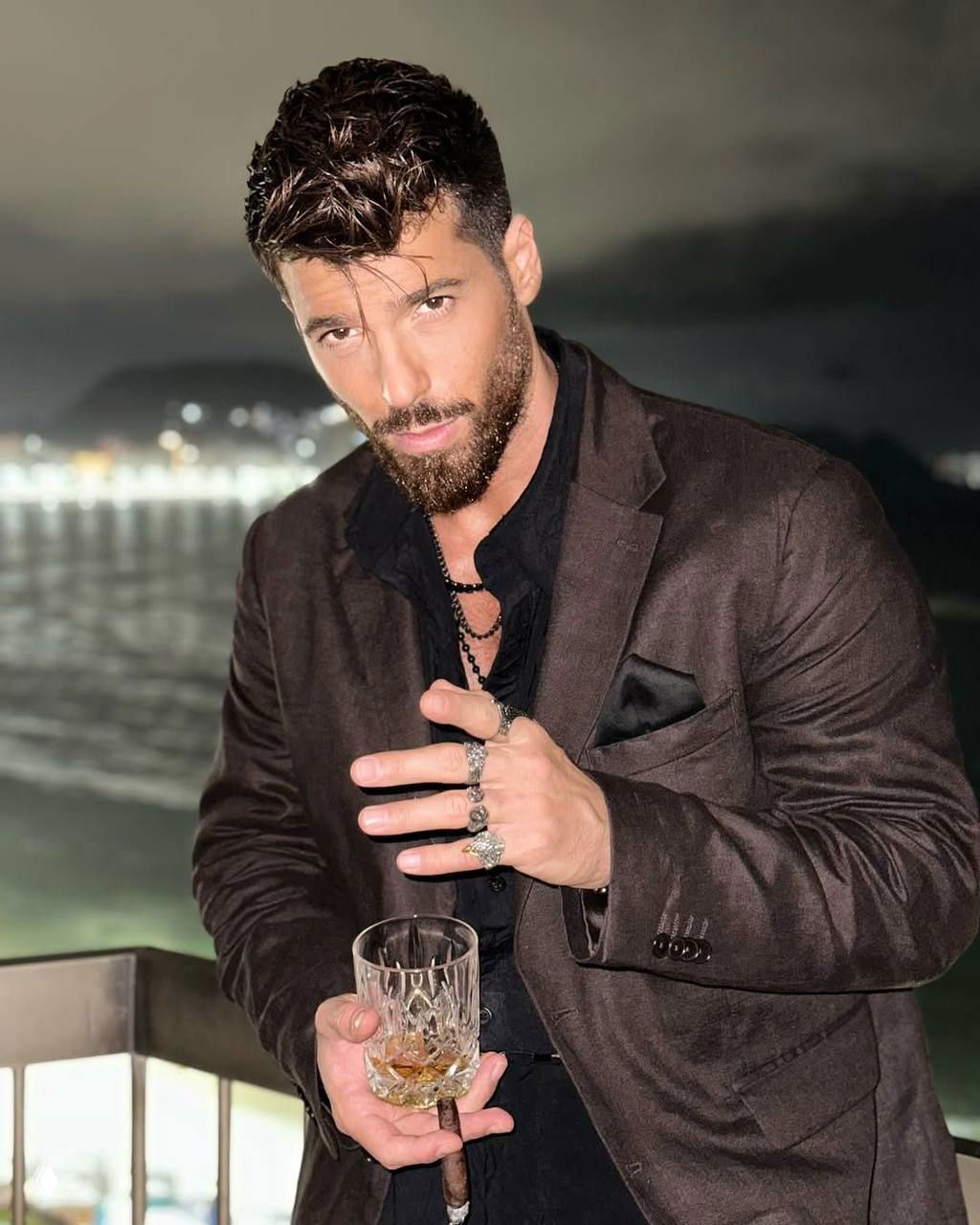 Портрет Джина Ямана в тёплой подсветке держит стакан и сигару; кадр атмосферный, актёр в пиджаке на фоне ночного пейзажа у воды.