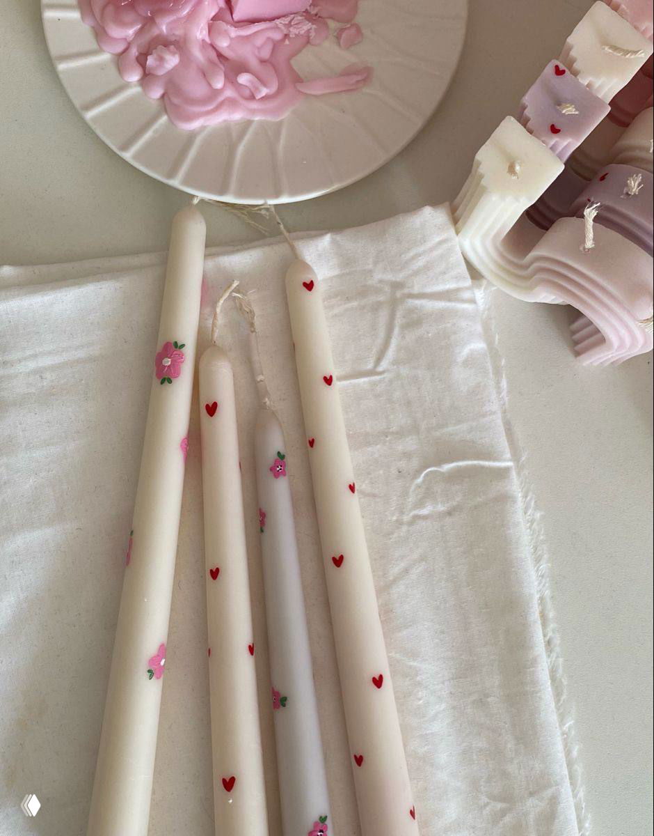 Крупный план нескольких пастельных свечей с точечной росписью сердечек и цветочных мотивов на хлопковой ткани — подготовка к декору