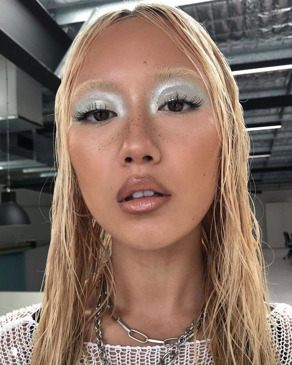 Портрет крупным планом девушки с серебристым теневым макияжем и глянцевыми губами; подчеркнуты ресницы и мягкий хайлайтер на скулах.
