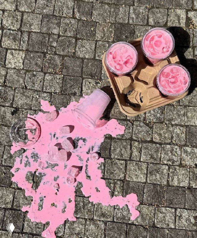 Розовый напиток с кусками льда пролился на брусчатку рядом с лотком, в который поставлены четыре одноразовых стакана — уличная сценка.