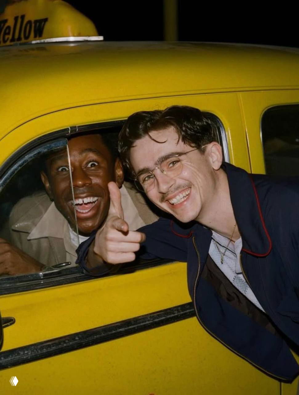 Ночное фото: два человека в желтом такси улыбаются в кадре, мужчина в окне машины и спутник создают атмосферу весёлой поездки по городу.