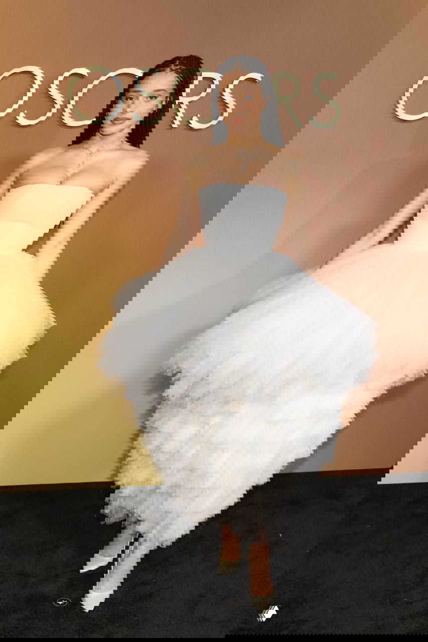 Женщина в пышном белом платье-пачке на красной дорожке Governors Awards, полный рост на фоне золотистого бэкграунда с логотипом, фотография с Governors Awards в Лос-Анджелесе.