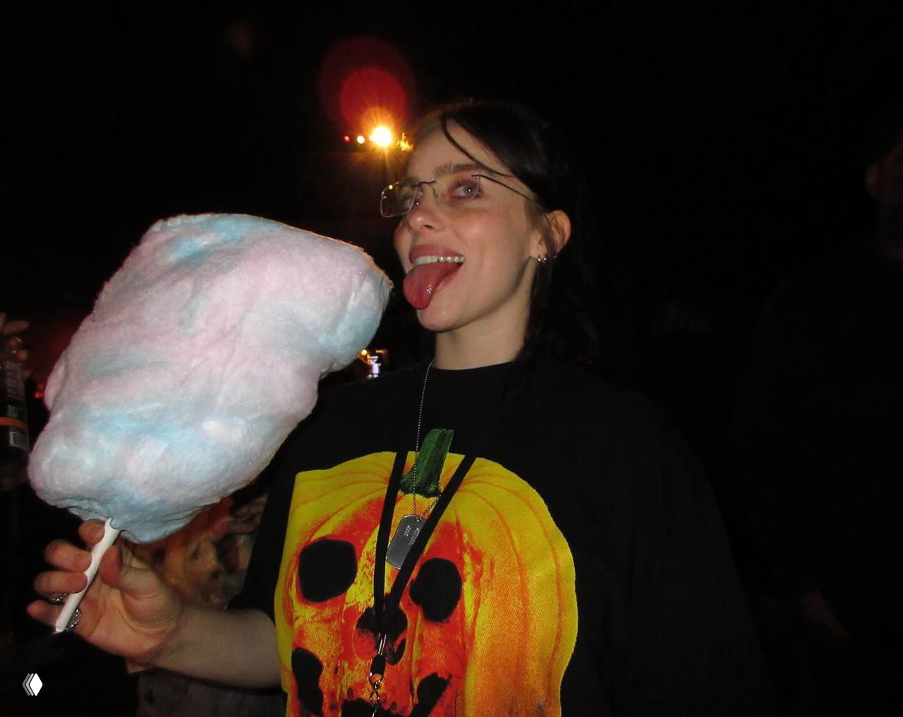 Момент из вечерней сцены: молодая женщина держит большую розово-голубую сладкую вату на палочке, тёмный фон и праздничная атмосфера.