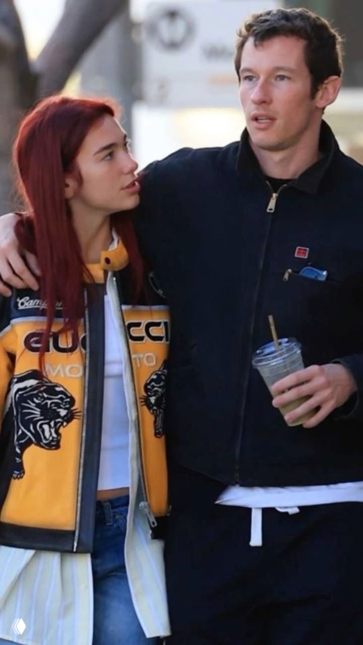 Мужчина и женщина прогуливаются, обнявшись: она в яркой куртке, он держит стакан с напитком, уличная сцена с размытым фоном