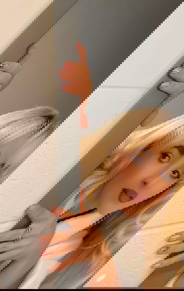 Фото: женщина выглядывает из‑за двери; розово‑нюдовые ногти с небольшим красным акцентом на безымянном пальце, руки в фокусе.