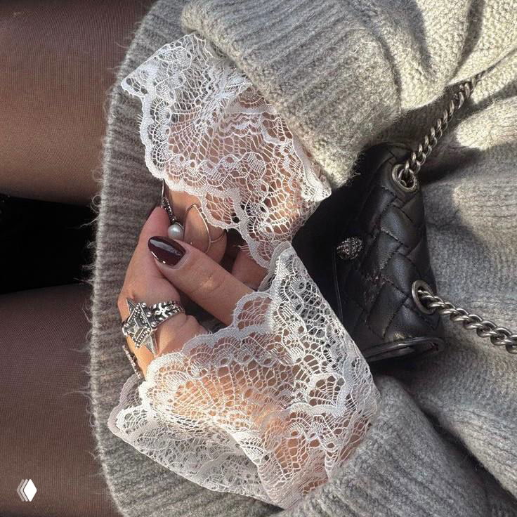 Руки в вязаных перчатках с кружевными манжетами и массивными кольцами — детали образа в мягкой серой гамме, элегантная текстурная эстетика.