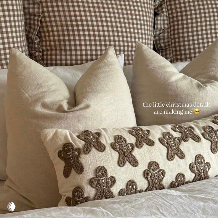 Подушки и декоративная подушка с пряничными мотивами на кровати — уютный интерьерный кадр в теплых бежевых тонах и новогодней стилистике.