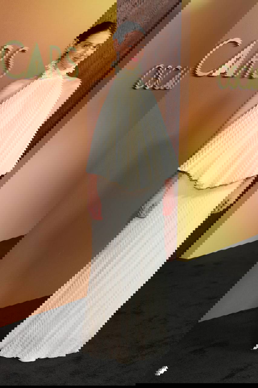 Женщина в плиссированном белом макси-платье с высоким воротом на красной дорожке Governors Awards, снята в полный рост на фоне бэкграунда, фотография с Governors Awards в Лос-Анджелесе.