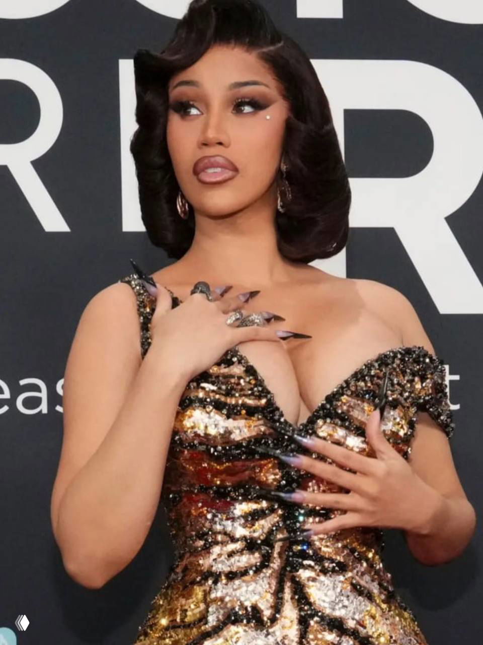 Артистка в блестящем декорированном платье на красной дорожке, крупный план лица и торса; заметны аксессуары и длинный маникюр.