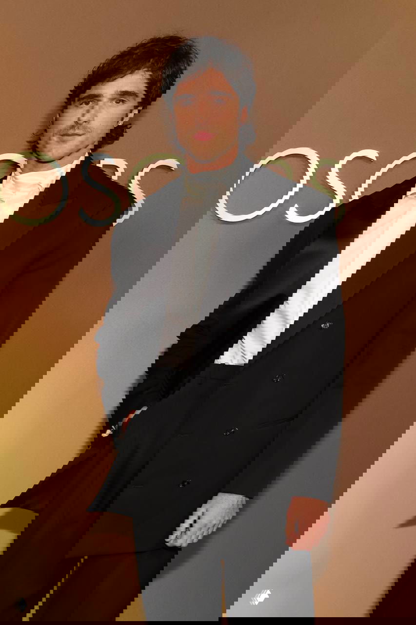 Мужчина в чёрном костюме и белой рубашке на красной дорожке Governors Awards, формальный образ на фоне золотистого бэкграунда и логотипа мероприятия, фотография с Governors Awards в Лос-Анджелесе.