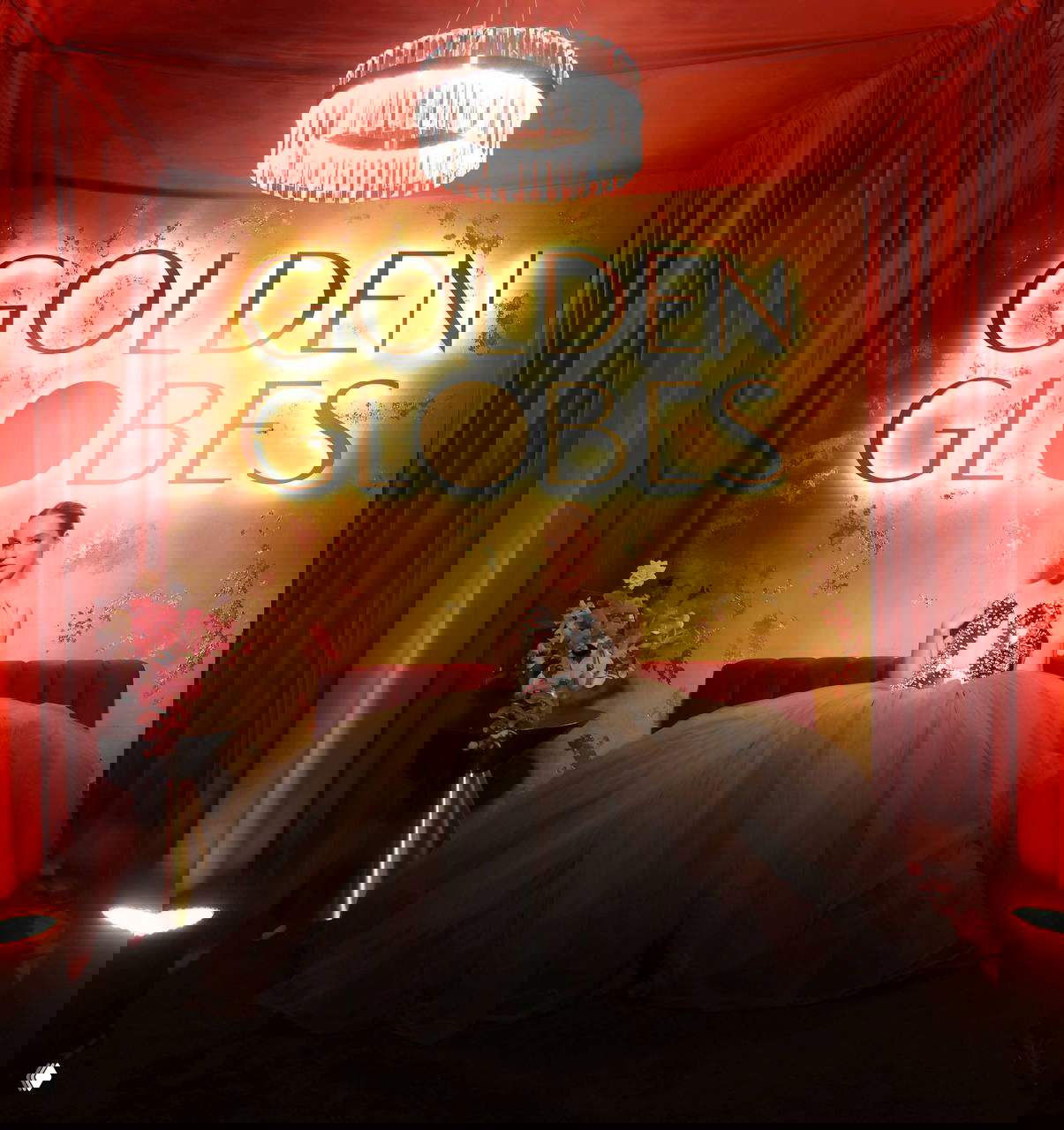 Фотозона с золотым фоном и надписью «GOLDEN GLOBES»: женщина в пышном платье позирует под люстрой на фоне красных занавесей и композиции цветов.