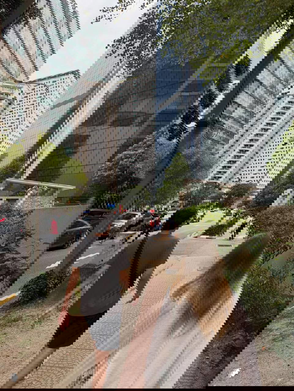 Прогулка по улице Куала‑Лумпура: пара идёт по тротуару на фоне современных многоэтажных зданий и городской среды.