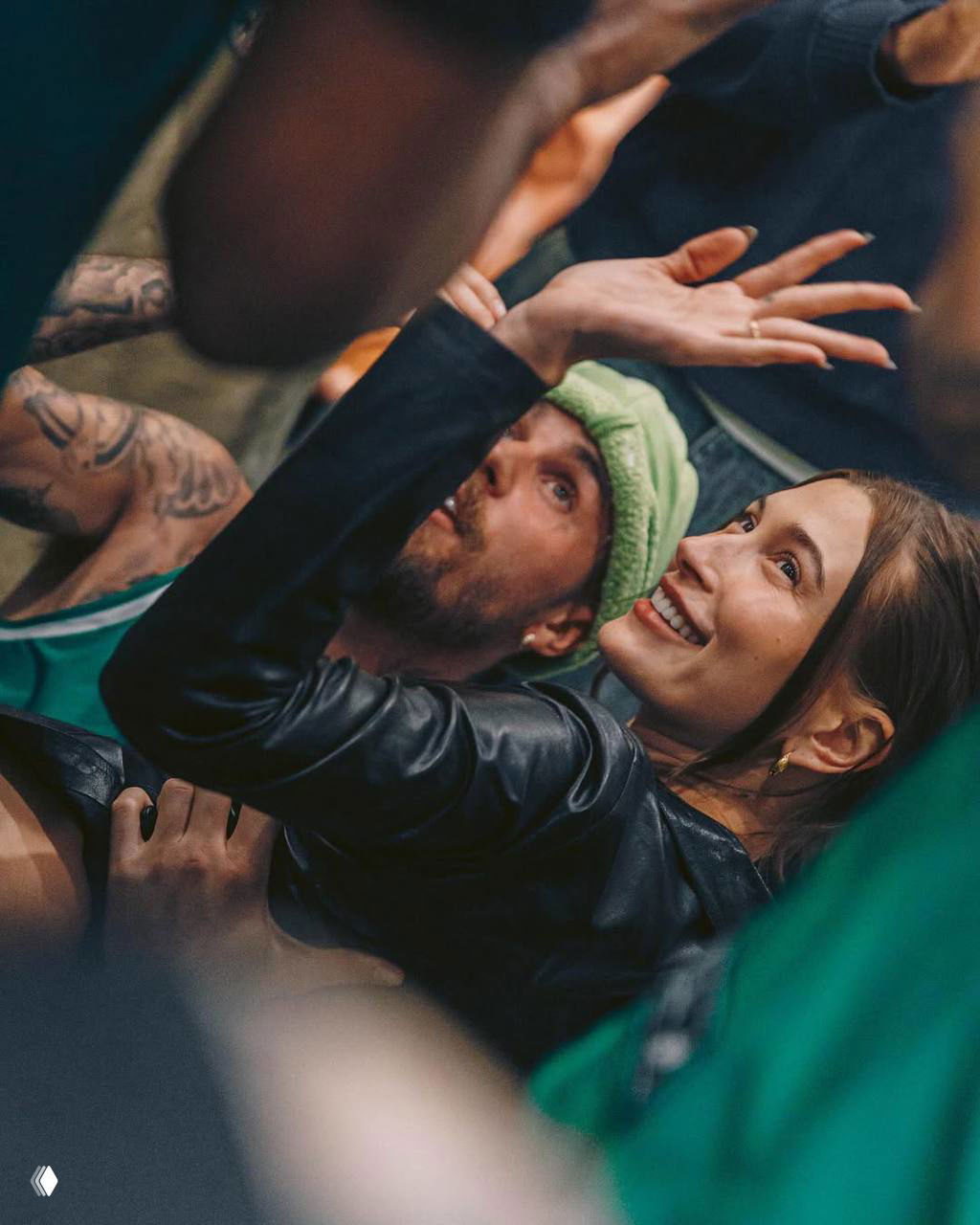 Хейли и Джастин Бибер на людном мероприятии: Хейли смотрит вверх и улыбается, вокруг люди и съемочная атмосфера, кадр крупным планом.