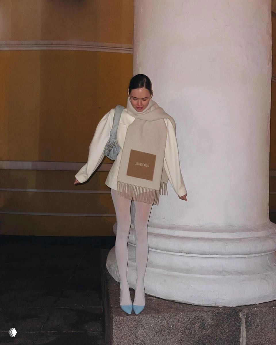 Уличный кадр: модель в светлом пальто и белых колготках, мини‑юбка и голубые лодочки — зимний нежный образ на фоне колонны городской архитектуры