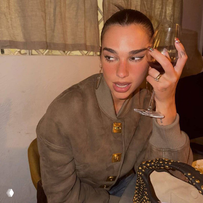 Полубоковой портрет Дуа Липы: рука у лица, виден сложный нейл-арт с кольцами, блёстками и декоративными элементами на ногтях.