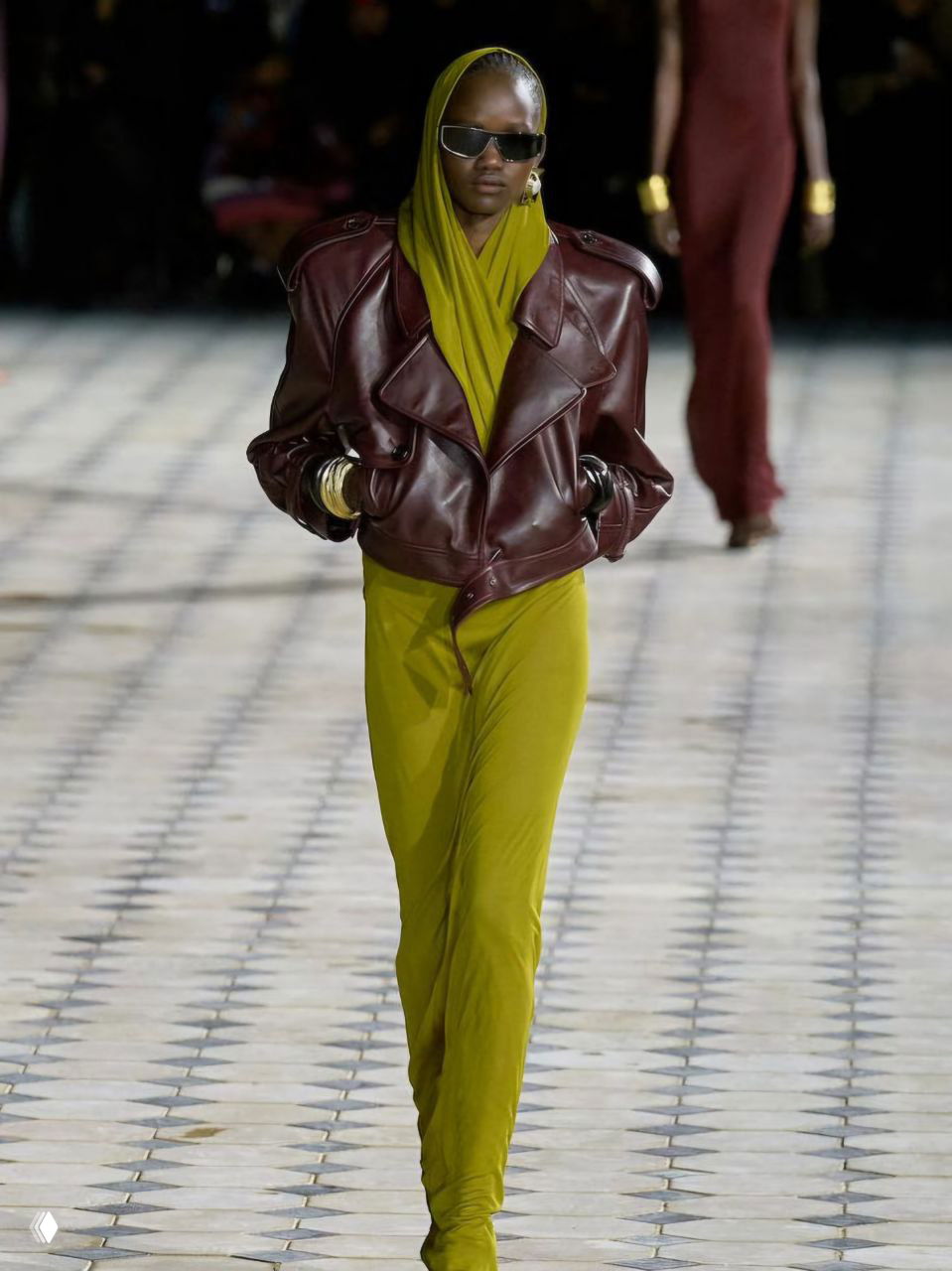 Подиумный образ: модель в бордовой кожаной куртке и оливково‑зелёном облегающем костюме, демонстрация сочетания зелёного и бордо в высоком модном ключе.