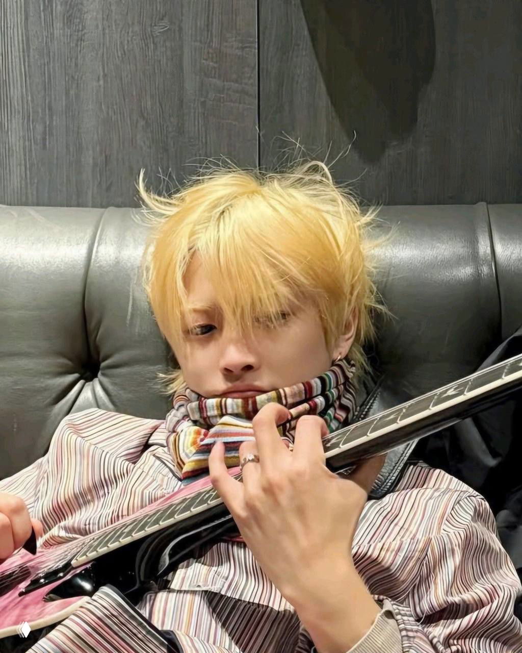 Хонджун с светлыми волосами лежит на диване с гитарой, крупный план рук и струн, расслабленная непринуждённая поза музыканта.