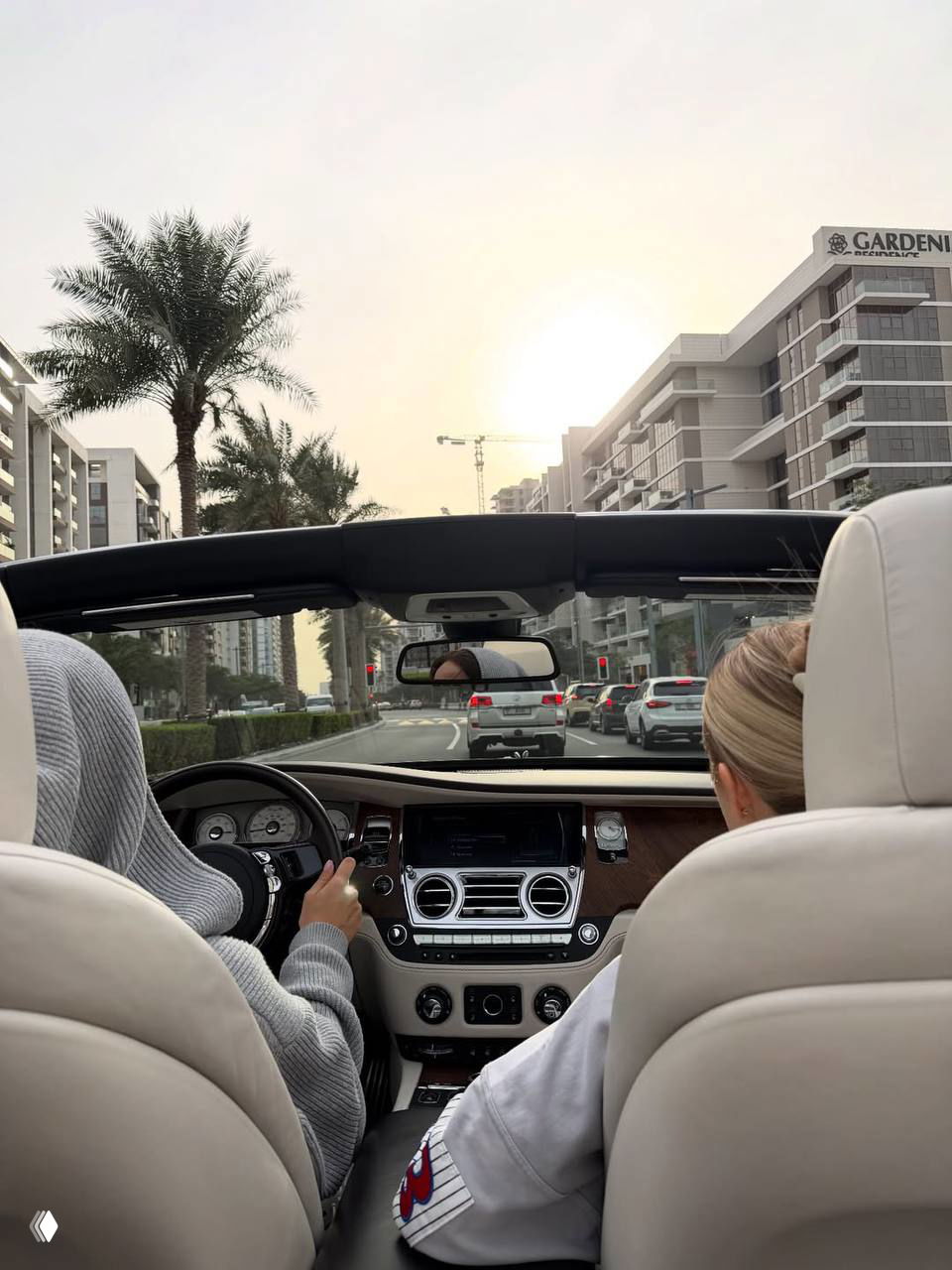 Вид из салона кабриолета по улицам Дубая: рулевое колесо, пассажиры и панорама жилых комплексов под вечерним небом.