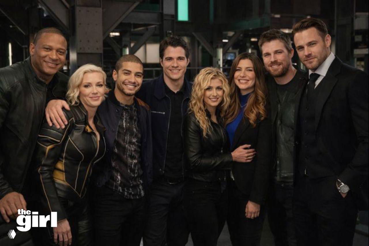 Группа героев в студии и костюмах боевика/приключения, мужчина в костюме стоит справа — коллективный постер, ощущение команды супергероев.