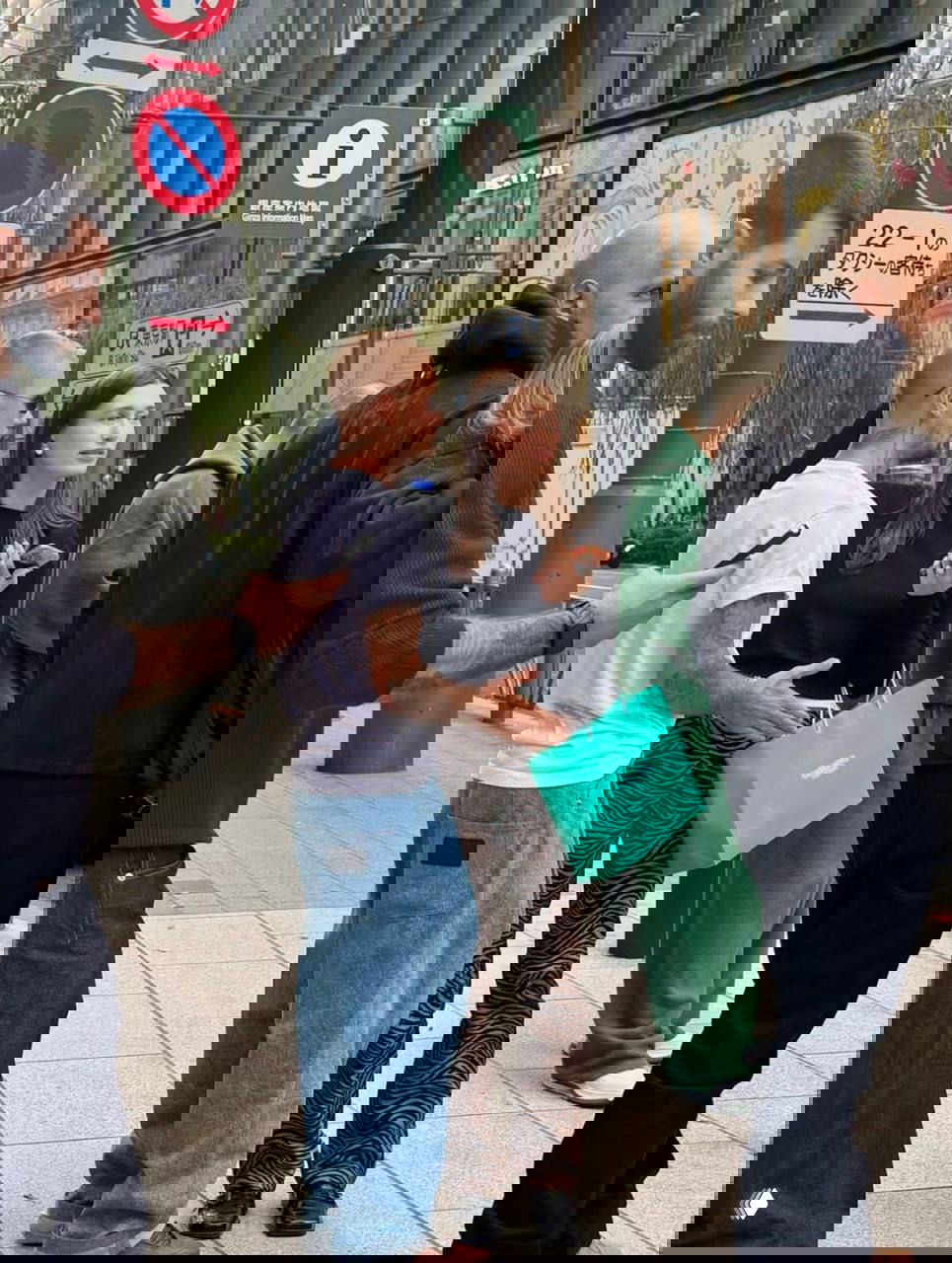 Уличный снимок в районе Гиндза: мужчина с татуировками в белой футболке и женщина в зебровых брюках держат бирюзовый пакет на тротуаре среди прохожих.